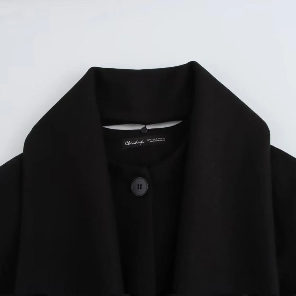 Women's long black coat with a grey artificial fur collar and front pockets.