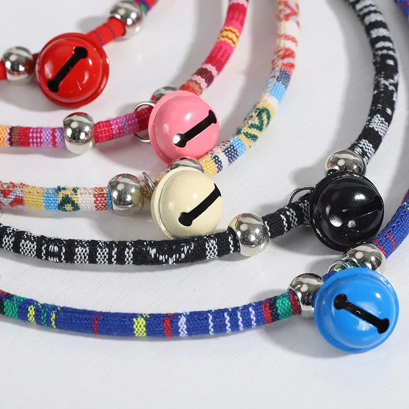 Coloured adjustable nylon pet collar with a metal buckle and brass bell in black, blue, pink, red, and white options.