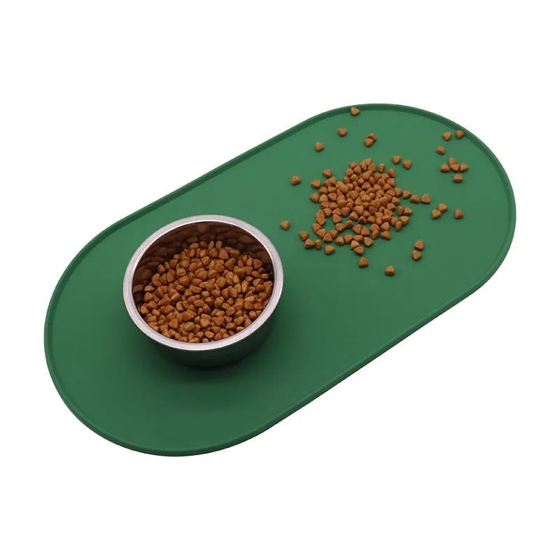 Green silicone cat feeding placemat with food and water bowls on top on a wooden floor.