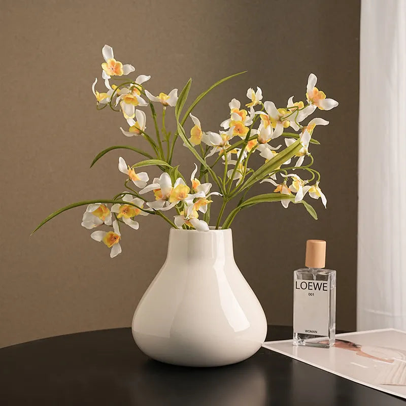Black ceramic modern vase with white artificial orchid stems on wooden table