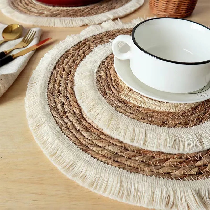 Round natural papyrus straw placemat with tassel detailing on a table.