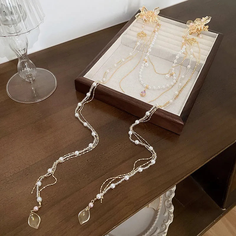 Gold women's hairpin with acrylic pearl flower, long tassels, and diamond-bead grip on a metallic pin.
