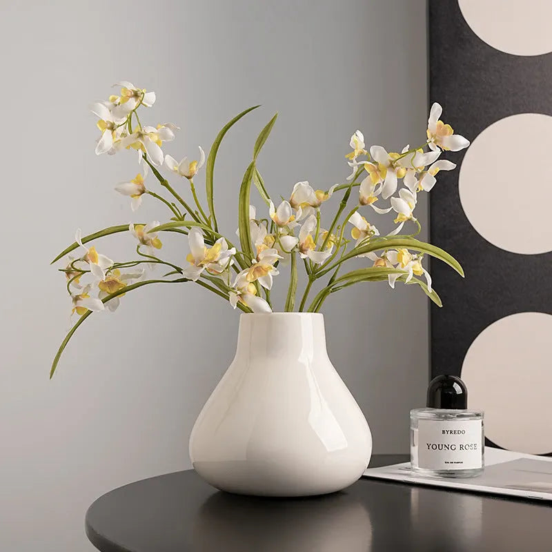 Black ceramic modern vase with white artificial orchid stems on wooden table