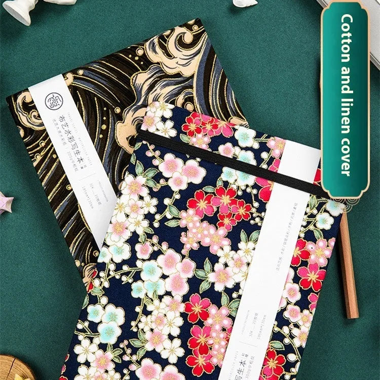 Feiluniao handmade fabric watercolour notebook open on a table with paints, showing a decorative cover.