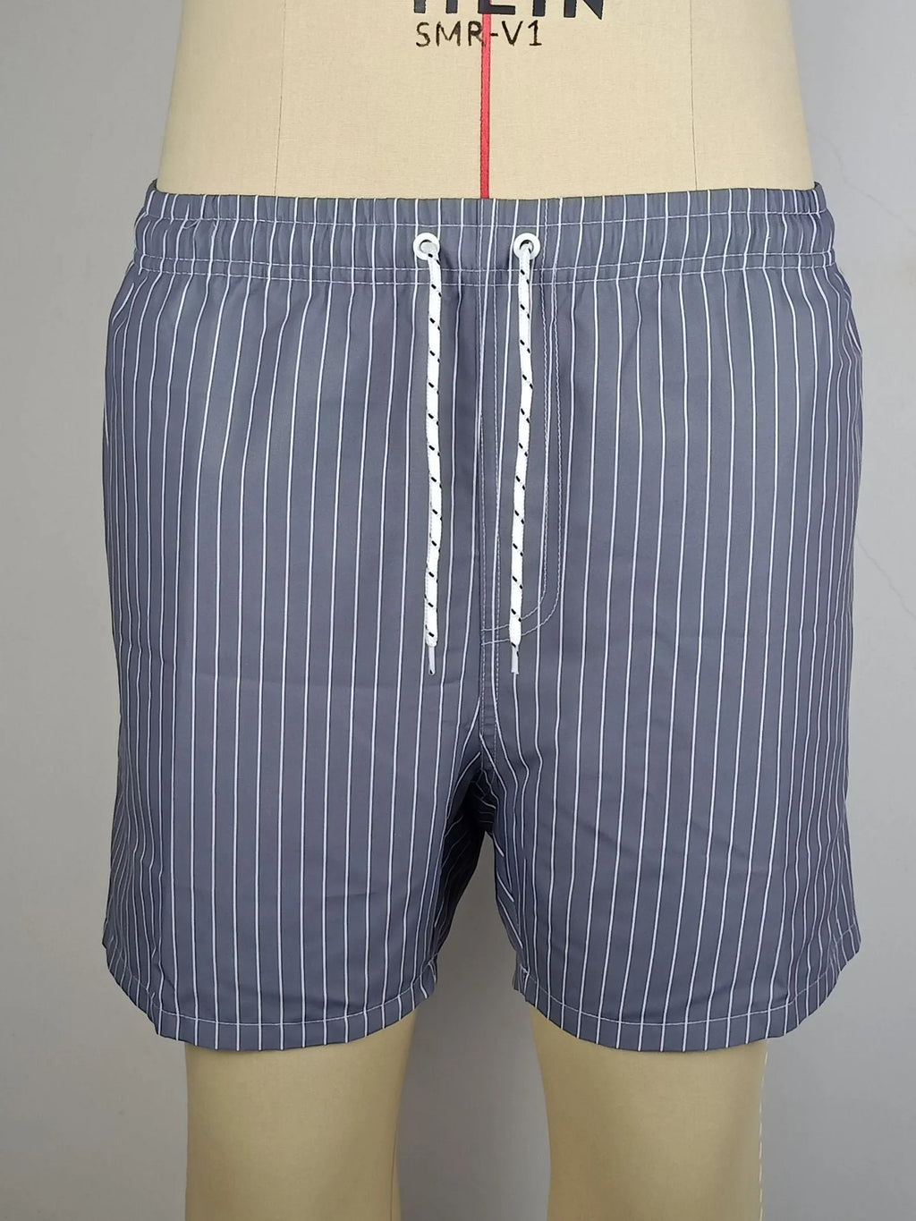 A man wearing grey striped polyester beach shorts with a straight leg opening, shown on a beach.