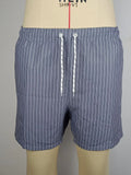 A man wearing grey striped polyester beach shorts with a straight leg opening, shown on a beach.