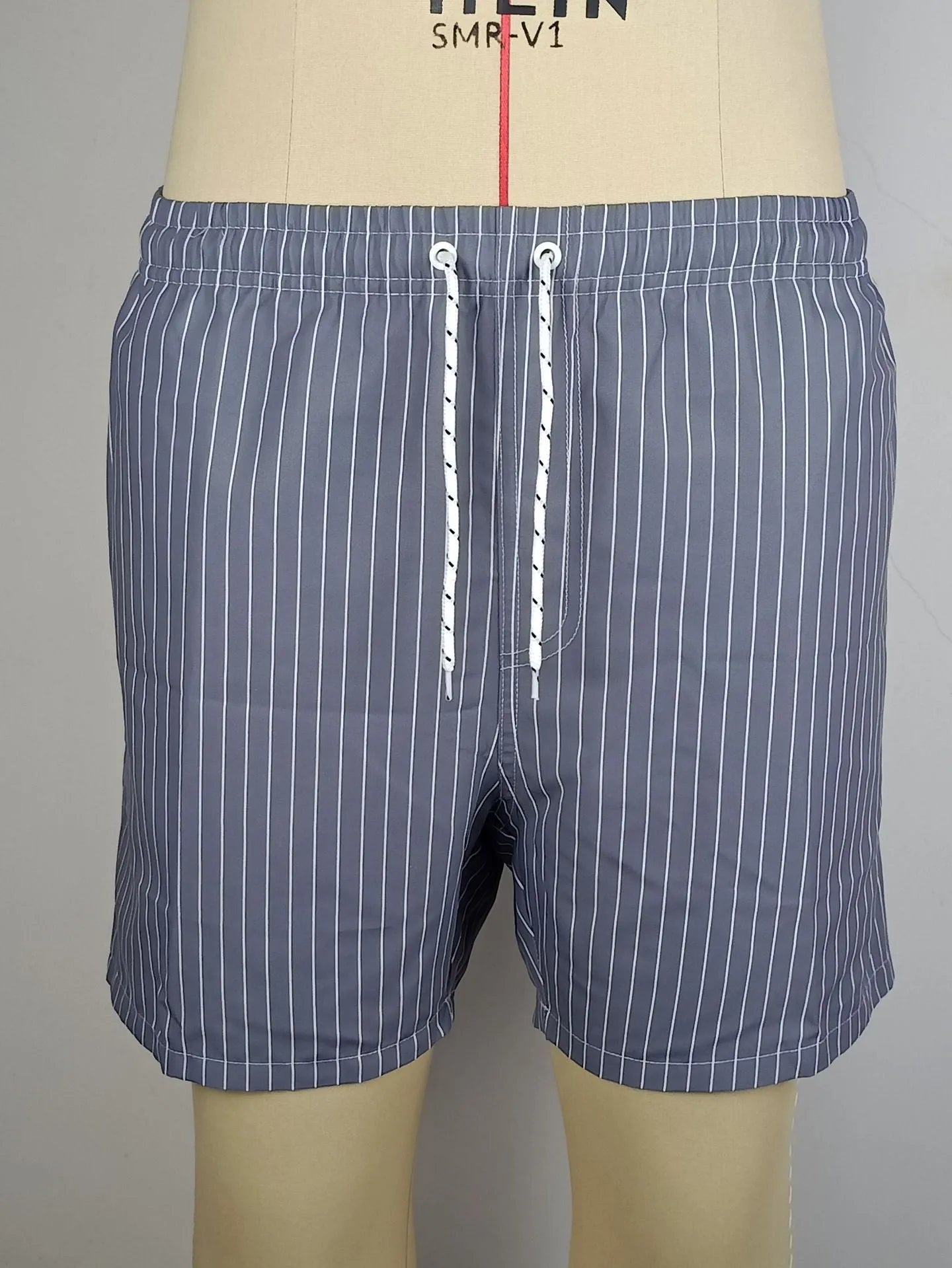 A man wearing grey striped polyester beach shorts with a straight leg opening, shown on a beach.