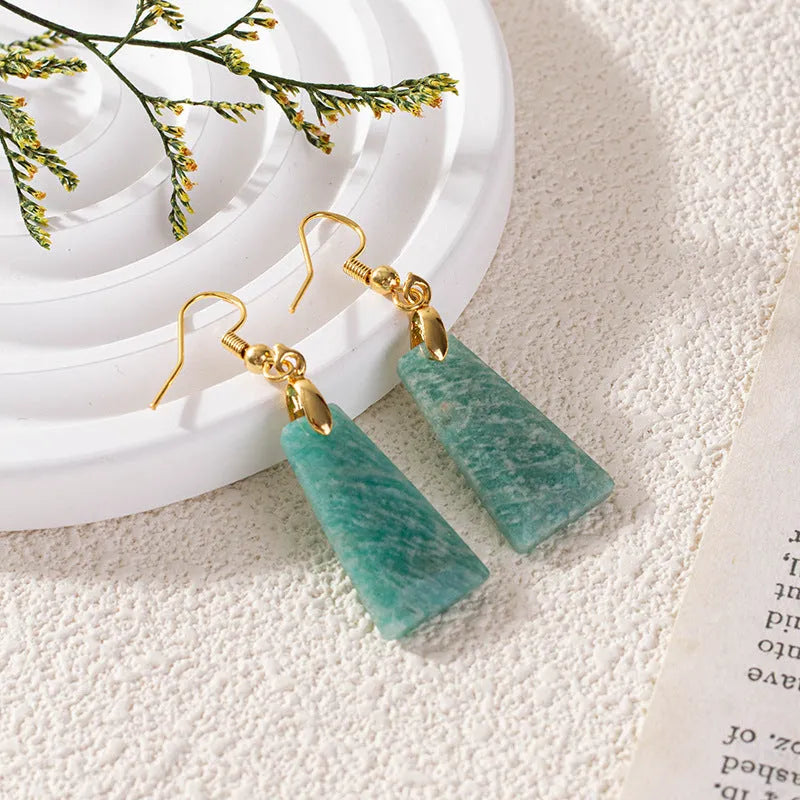 A pair of trapezoid-shaped rough amazonite earrings on a gold and silver background.