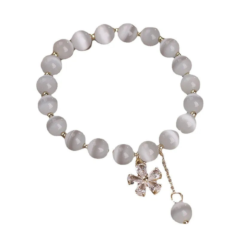 Women's single loop white cat's eye crystal bracelet with flower pattern and tassels, showing safety buckle clasp