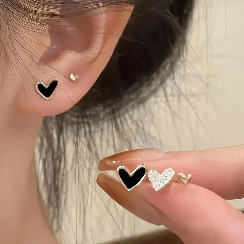 Set of three pairs of women's heart-shaped alloy earrings in gold, black, pink, and black-white colours.
