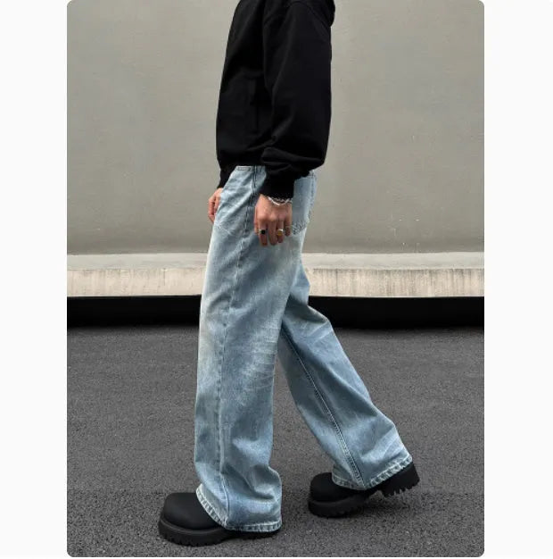 Man wearing blue straight leg jeans with whisker wash detailing and a flared leg style.
