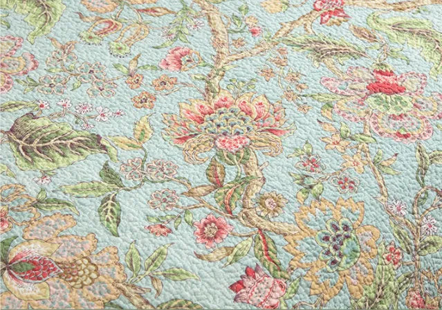 Blue botanical patterned quilted cotton bedspread set on a bed, showing plants, flowers, and bird design.