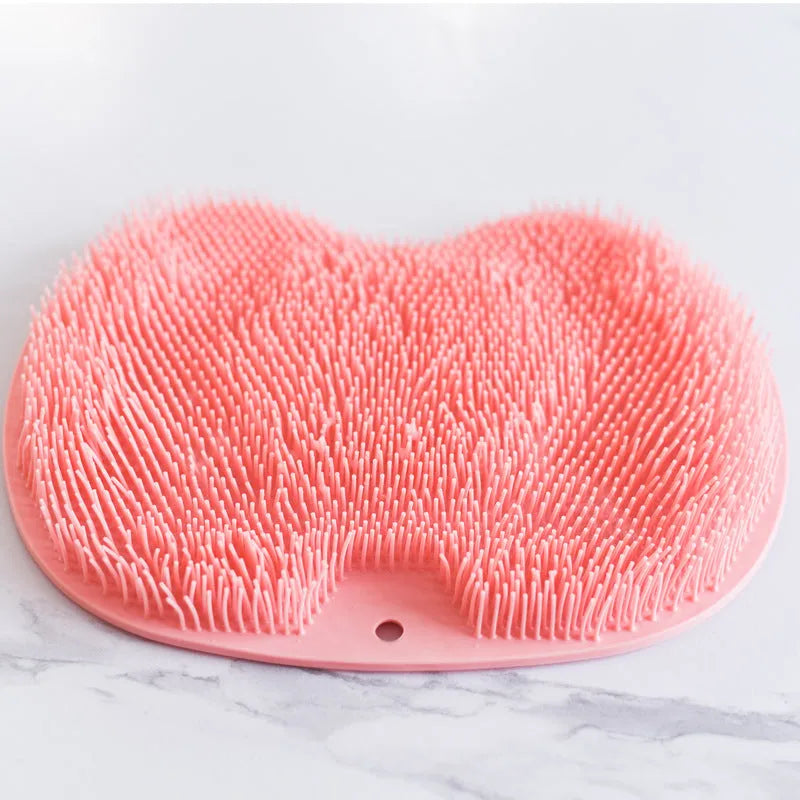 Orange silicone bristle bath brush with suction cup base on bathroom tiles.