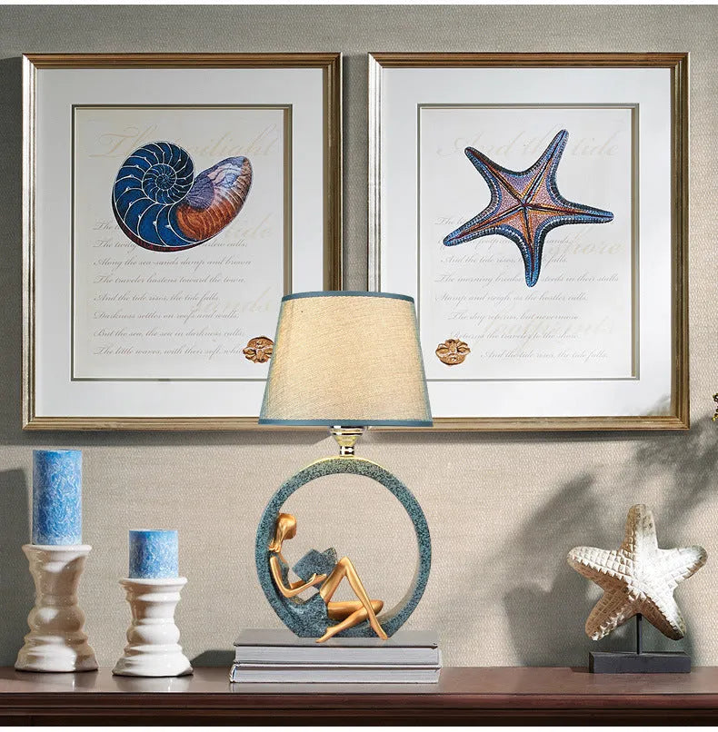 Blue resin reading girl table lamp with cloth shade on a table, 20x39.8cm