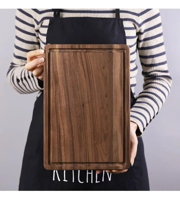 Black walnut wood chopping board with juice groove and side handle on kitchen counter