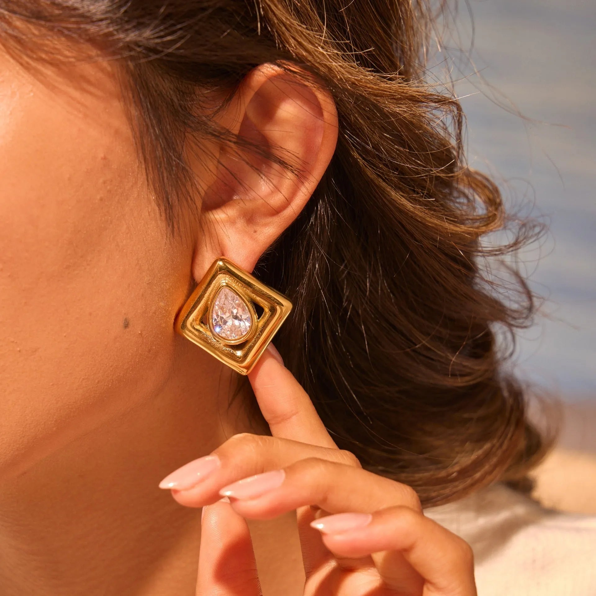 Geometric gold stud earrings with a water drop zircon stone inlaid in the centre.