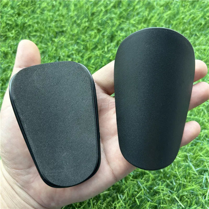 Extra small mini plastic football shin guards for kids in black and white, measuring 8 by 5 centimetres.