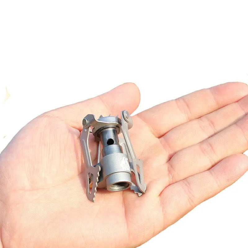 Portable camping gas stove with one-piece furnace on a rocky outdoor surface.
