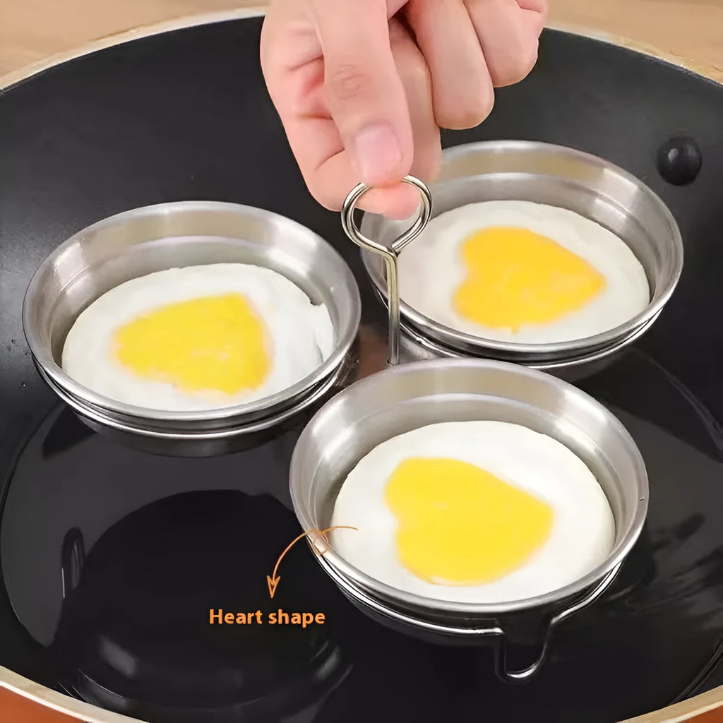 Stainless steel heart-shaped egg steamer next to a round model on a kitchen counter.