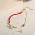 Gold and red women's bracelet with a silver peace buckle, red rope, and Hetian jade charm.