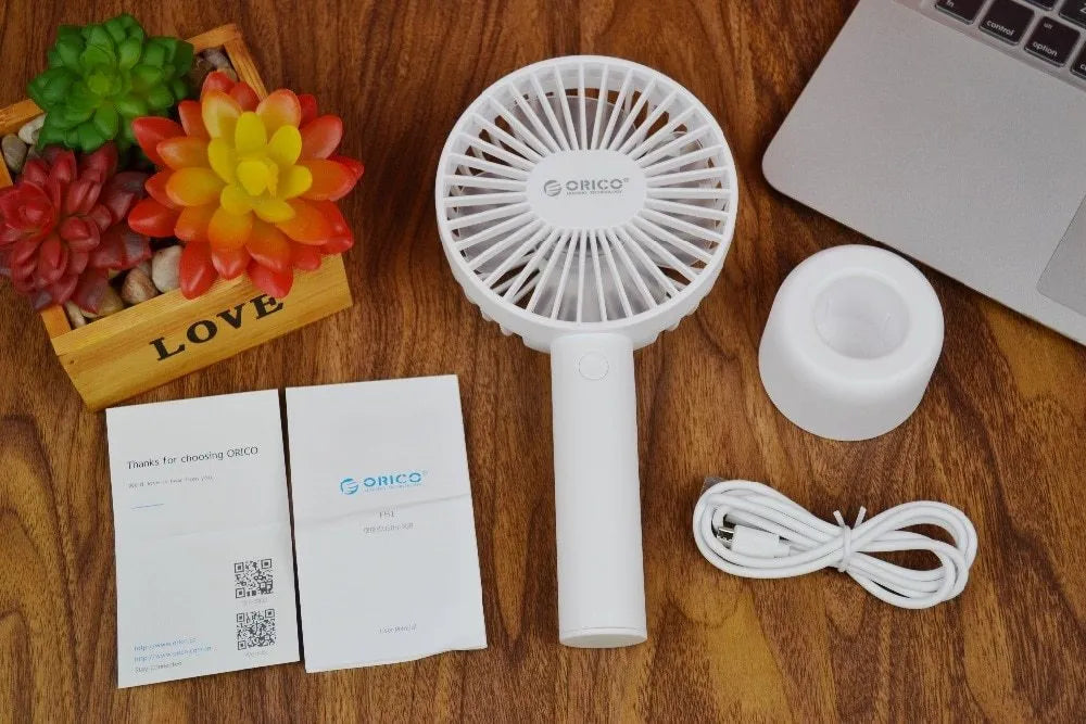 White ORICO FH1 handheld USB rechargeable desk fan with three-speed buttons on a desk.