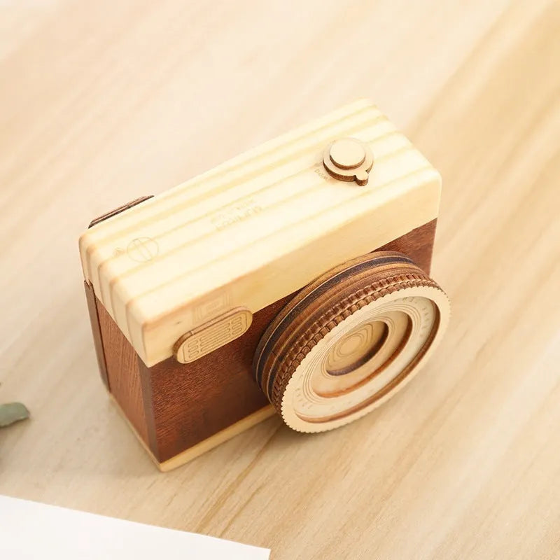 Small wooden camera-shaped music box with a rotating mechanism on a natural pine wood finish.