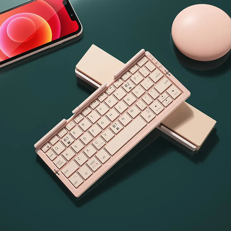 Silver white mini aluminium folding Bluetooth keyboard open next to a smartphone on its integrated stand.
