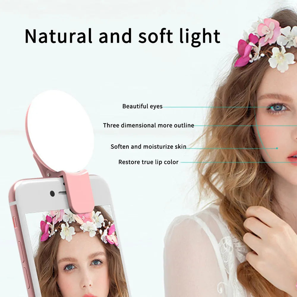 A small, round white clip-on LED fill light attached to a mobile phone for taking selfies.