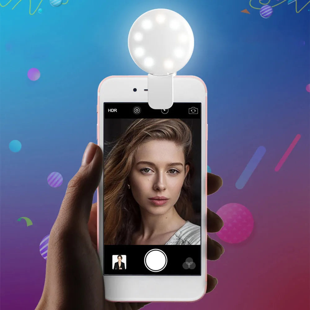 A small, round white clip-on LED fill light attached to a mobile phone for taking selfies.