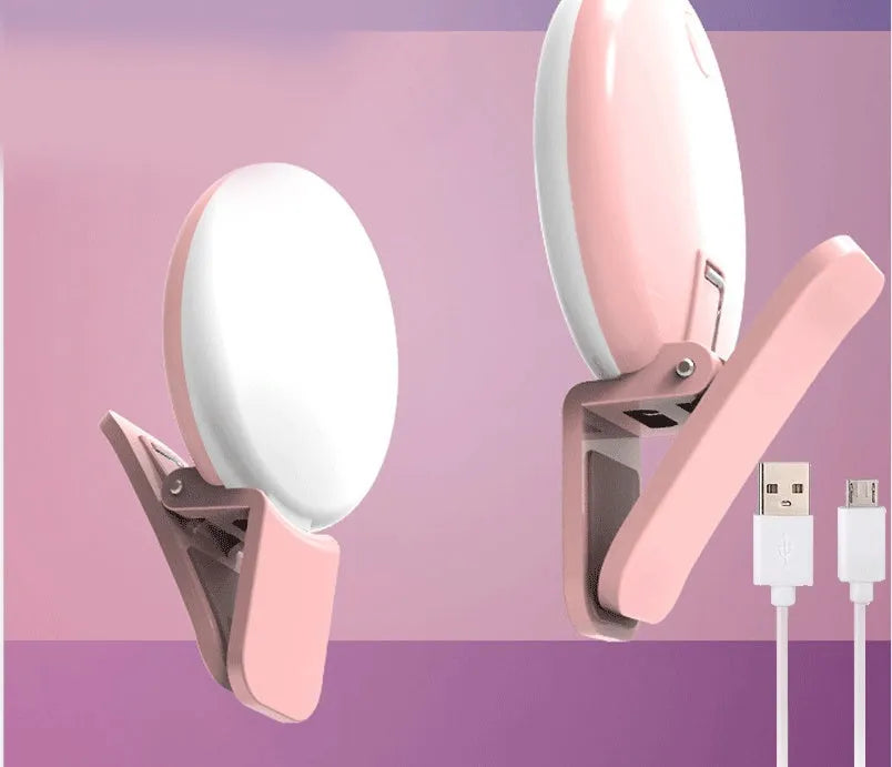 A small, round white clip-on LED fill light attached to a mobile phone for taking selfies.