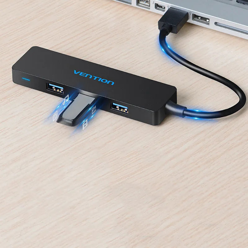 Black four-port USB 3.0 hub with a short cable on a desk next to a laptop.