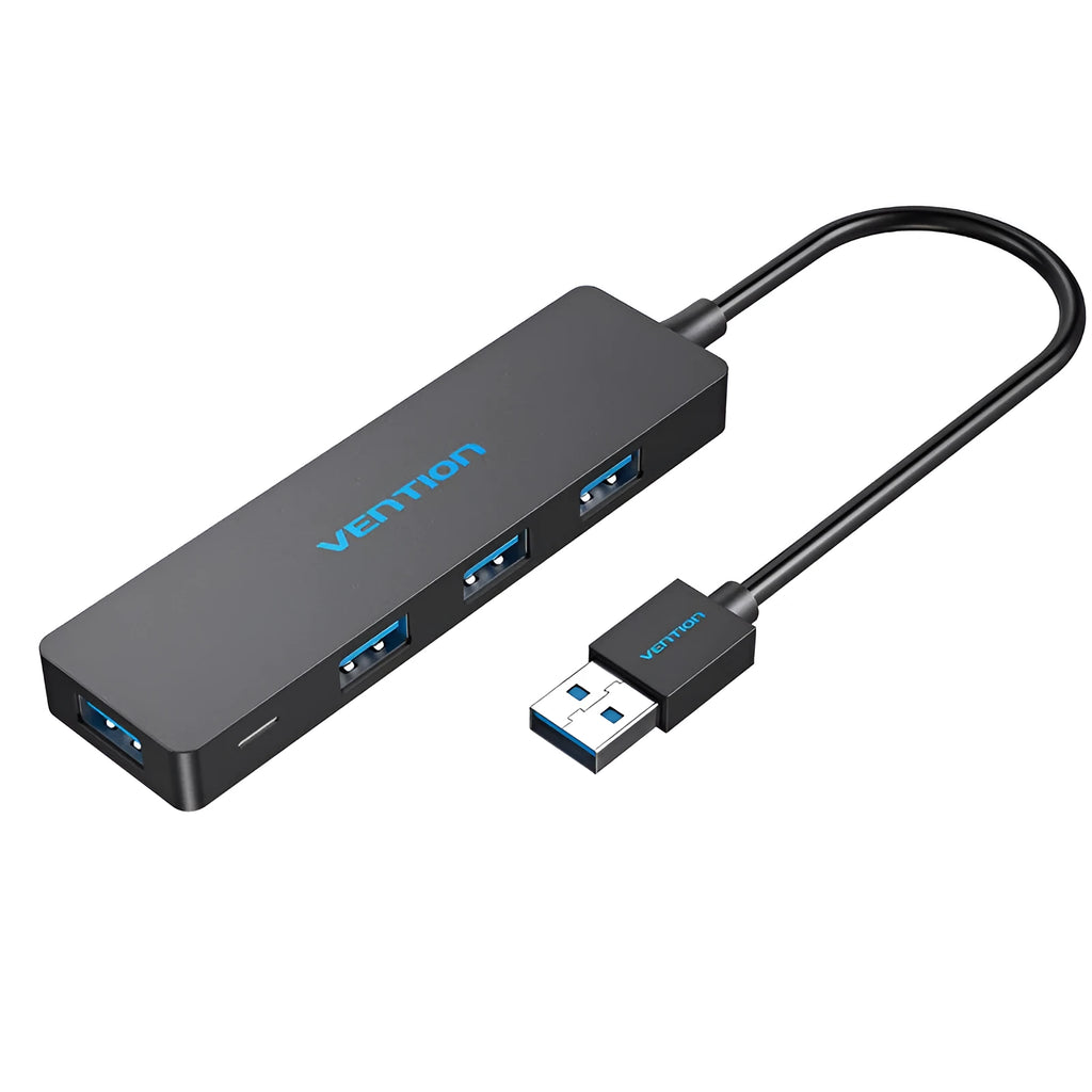 Black four-port USB 3.0 hub with a short cable on a desk next to a laptop.