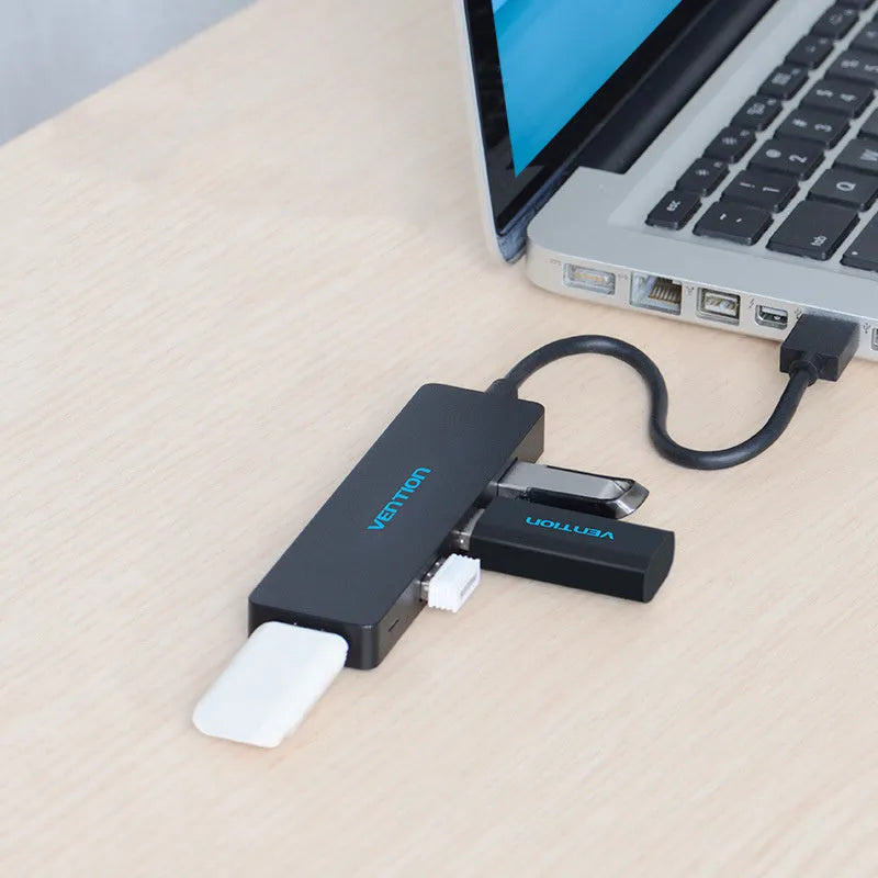Black four-port USB 3.0 hub with a short cable on a desk next to a laptop.