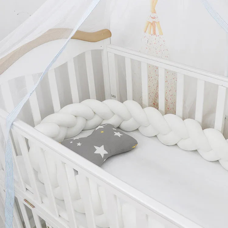 Braided knot design crib bumper in spandex velvet, shown in a light grey colour wrapped around crib slats.
