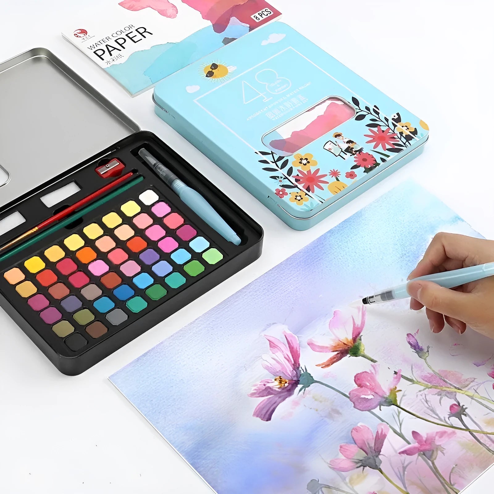 Metal tin open to show 48 pans of solid watercolour paint in various colours including black, pink, and blue.