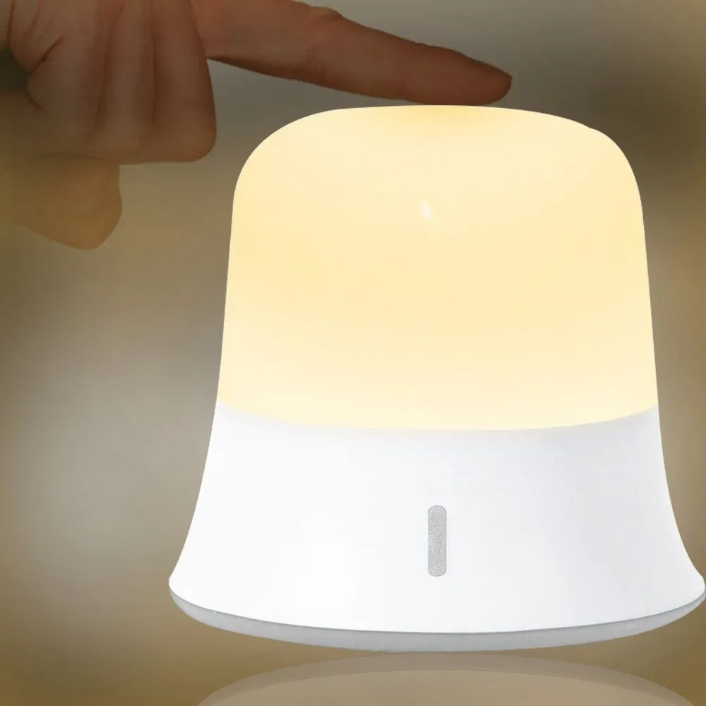 White rechargeable bedside night light with touch controls on a wooden table.