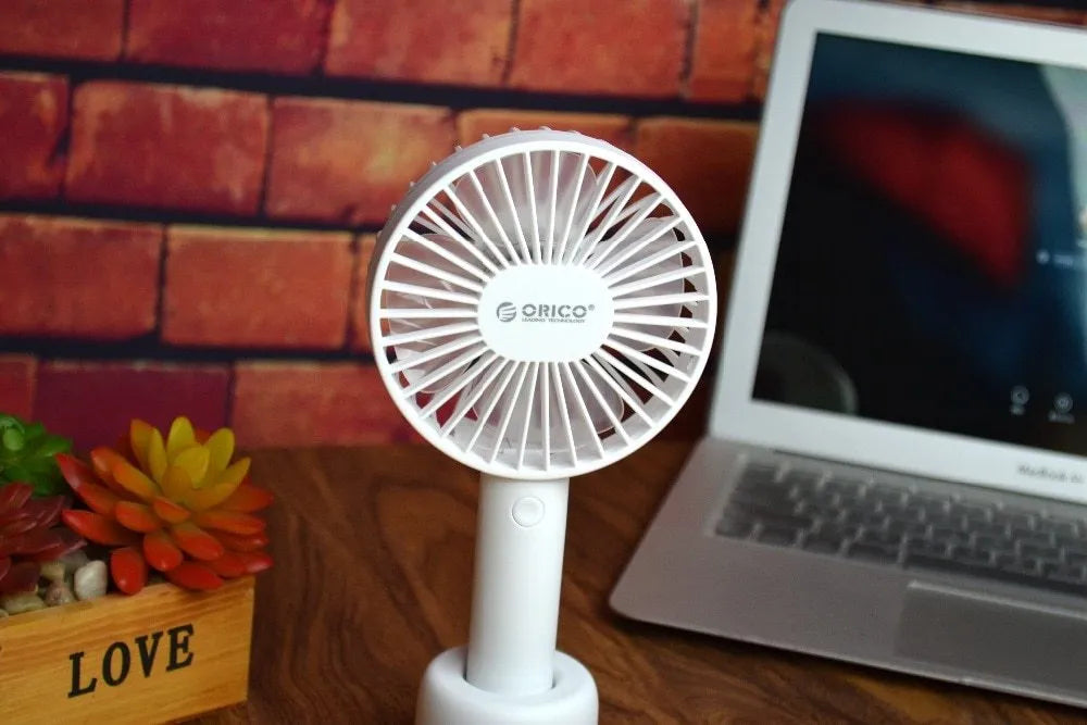 White ORICO FH1 handheld USB rechargeable desk fan with three-speed buttons on a desk.
