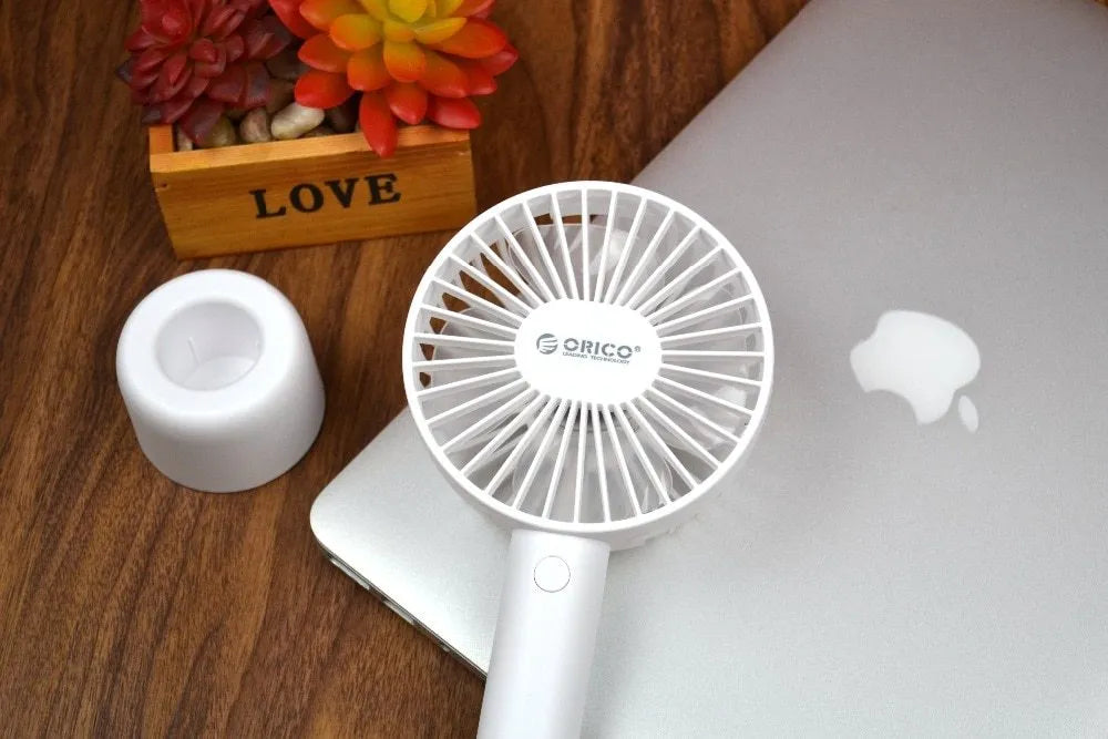 White ORICO FH1 handheld USB rechargeable desk fan with three-speed buttons on a desk.