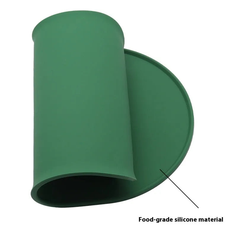 Green silicone cat feeding placemat with food and water bowls on top on a wooden floor.