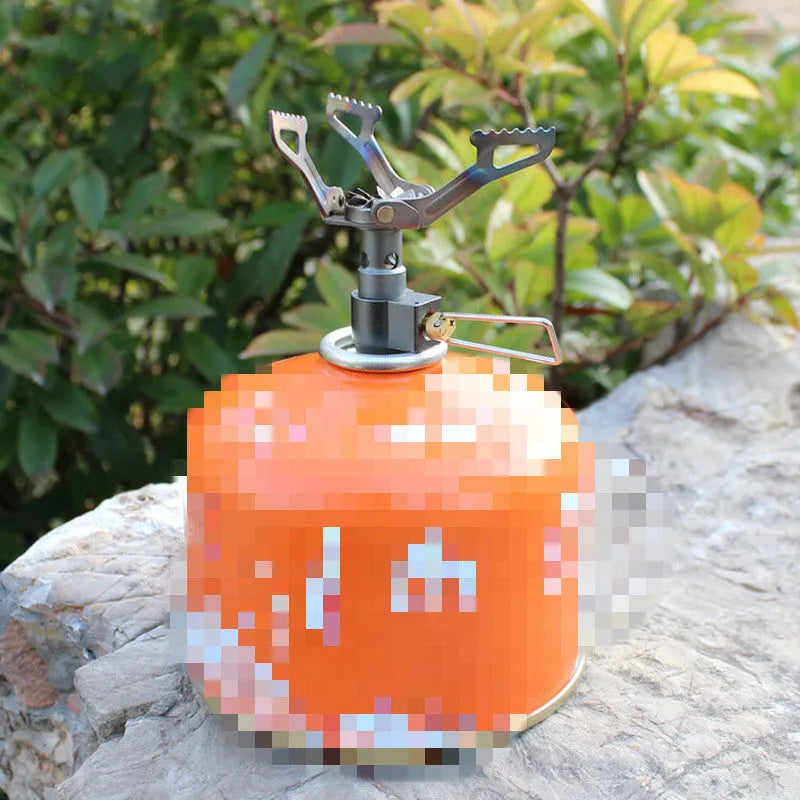 Portable camping gas stove with one-piece furnace on a rocky outdoor surface.