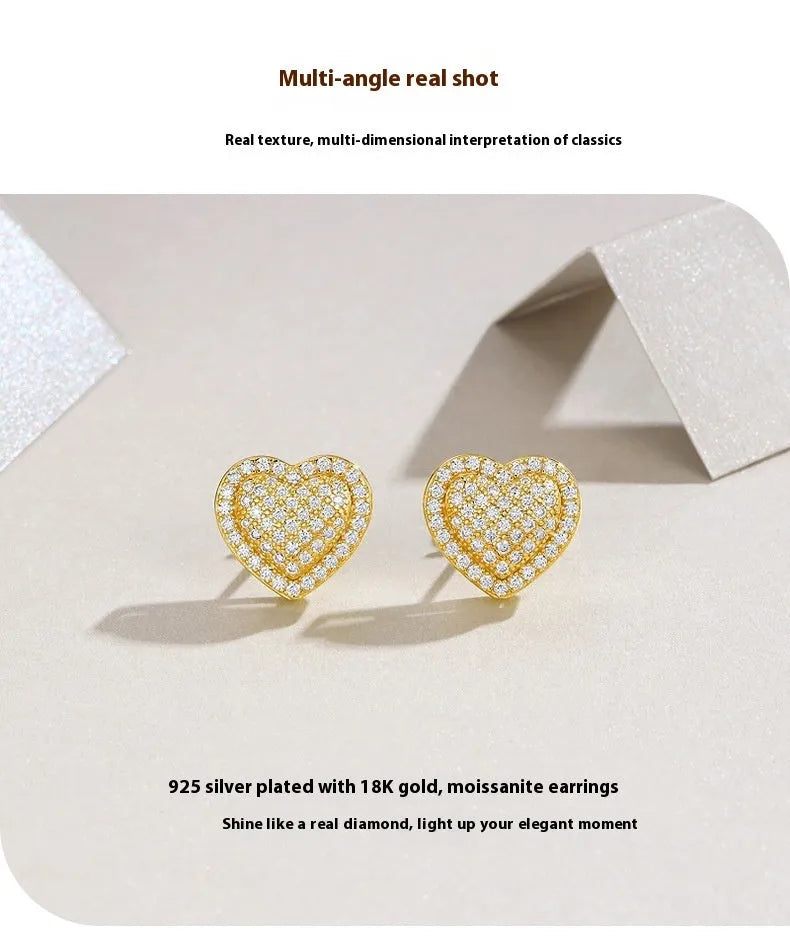 A pair of simple gold-tone heart-shaped stud earrings with a moissanite stone, shown from the front.