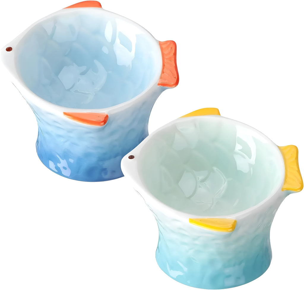 Four coloured fish-shaped ceramic pet bowls with a tilted, elevated design on a plain surface.