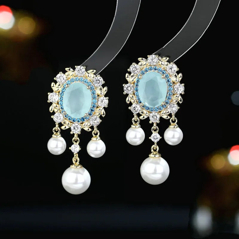 A pair of oval-shaped geometric drop earrings with a pearl tassel and zircon inlay on copper, shown in light purple.