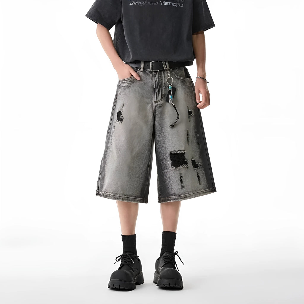 Grey loose fit denim shorts with distressed holes and a cropped length on a hanger.