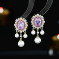 A pair of oval-shaped geometric drop earrings with a pearl tassel and zircon inlay on copper, shown in light purple.