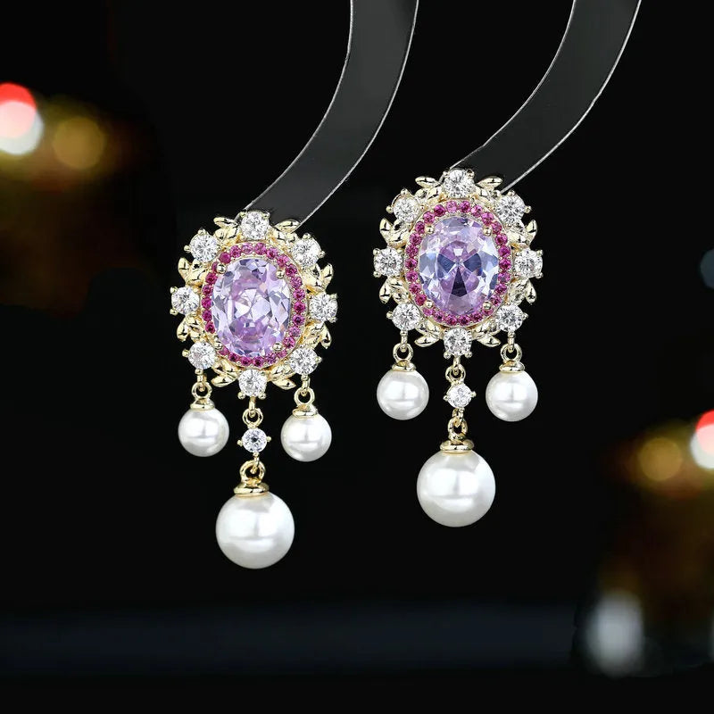 A pair of oval-shaped geometric drop earrings with a pearl tassel and zircon inlay on copper, shown in light purple.