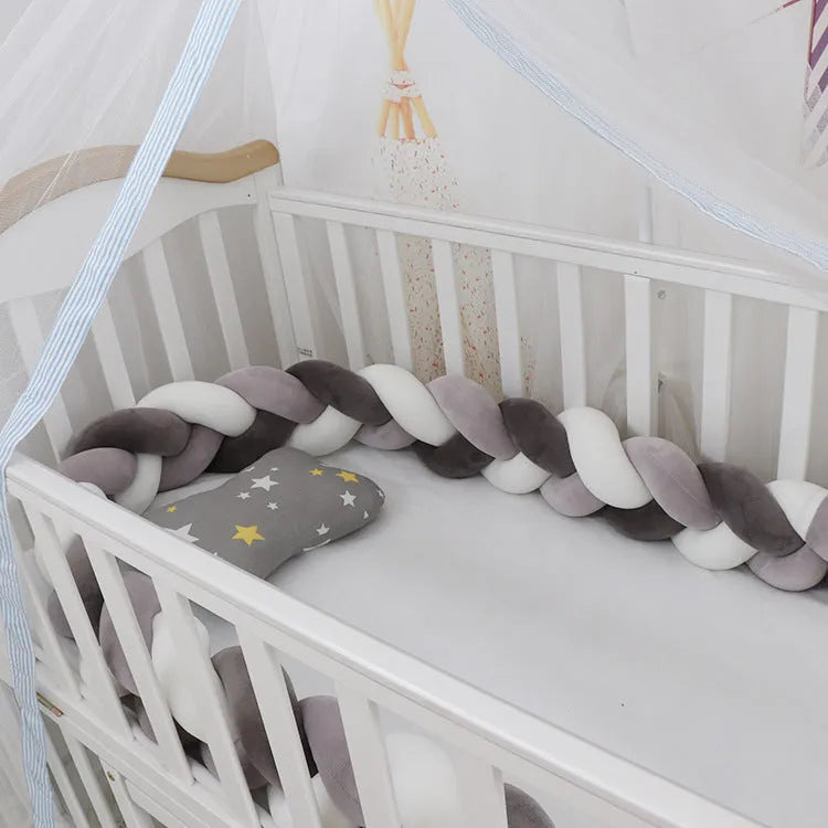Braided knot design crib bumper in spandex velvet, shown in a light grey colour wrapped around crib slats.