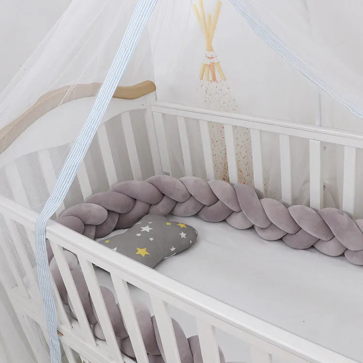 Braided knot design crib bumper in spandex velvet, shown in a light grey colour wrapped around crib slats.