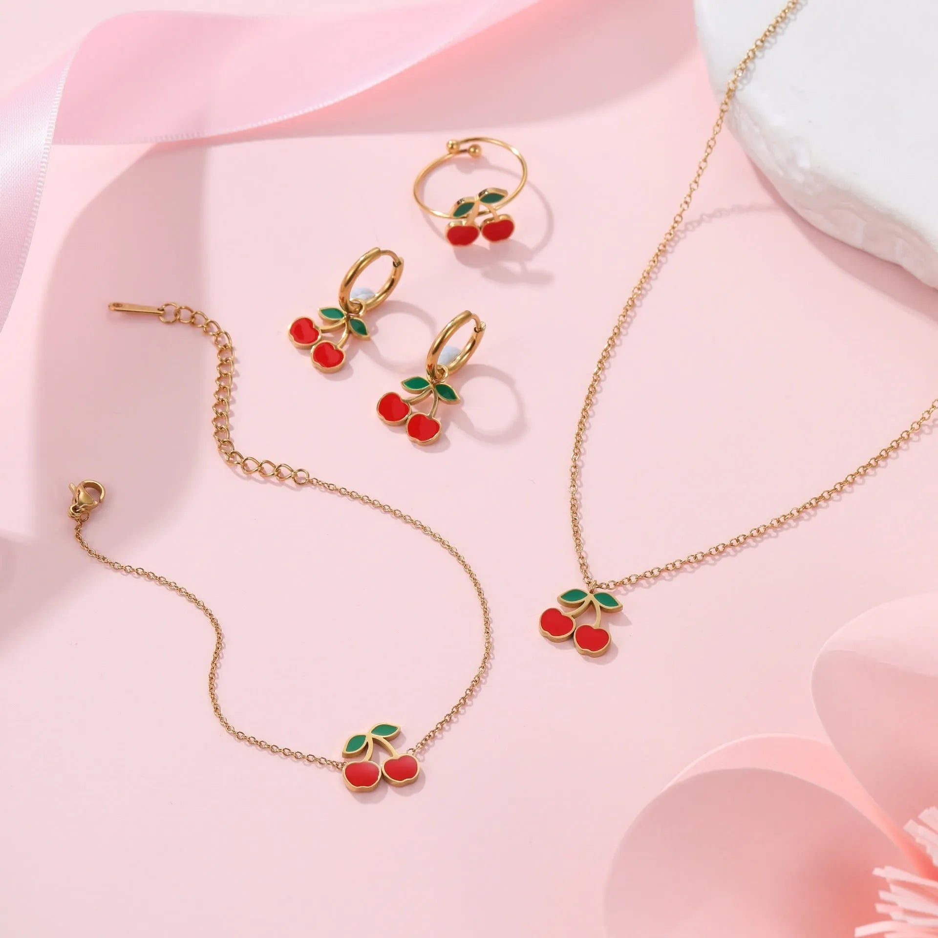 Cherry motif stainless steel jewellery set with gold plating, showing necklace, bracelet, earrings, and ring.
