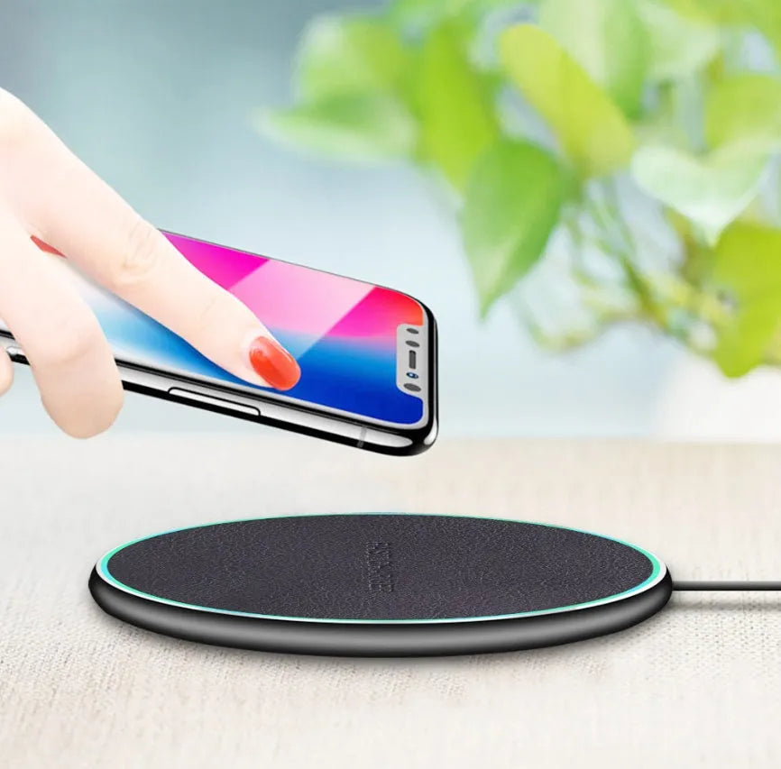 Black Quick Qi wireless charging pad on a desk, compatible with iPhone 11.
